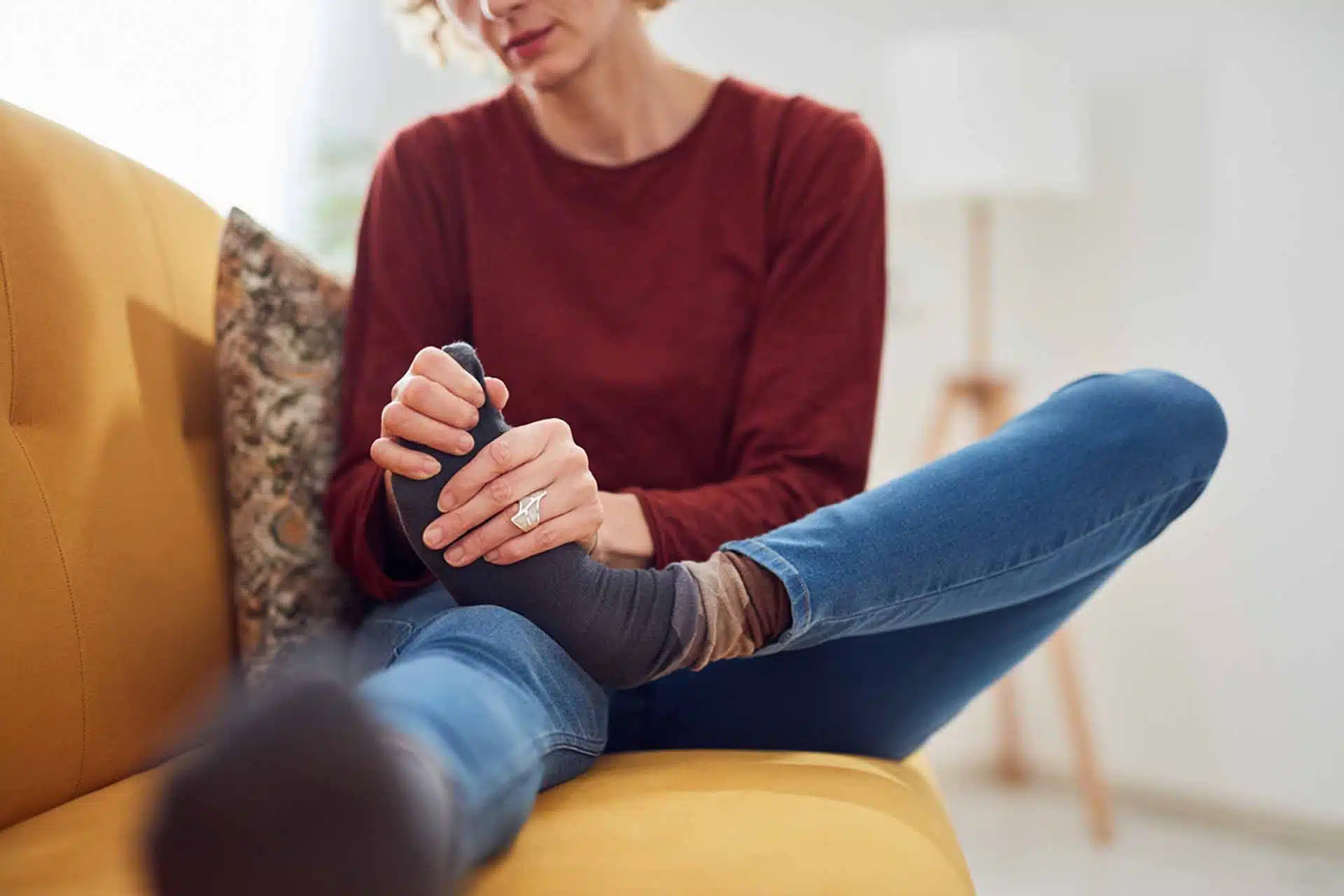 Woman holding her feet that suffers from intense pain sitting on a couch at home.