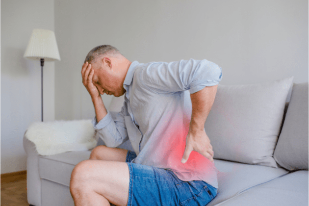 Man sitting on the couch holding his back feeling of too much pain caused by back pain.