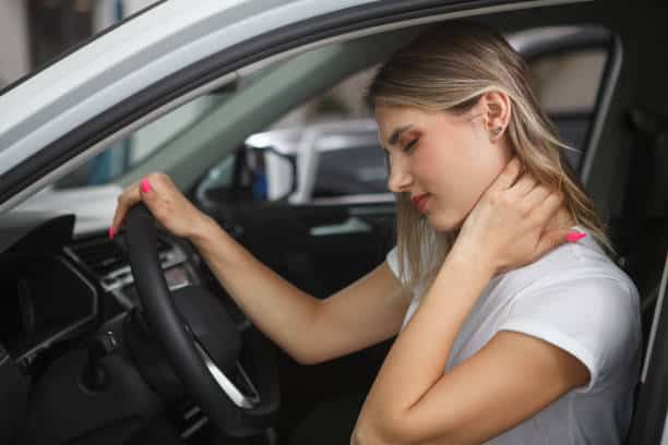 Young woman suffering from neck whiplash, sitting in drivers seat of her car.