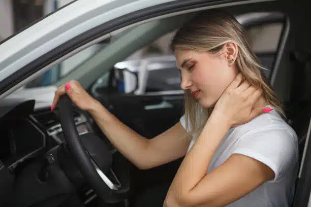 Young woman suffering from neck whiplash, sitting in drivers seat of her car.