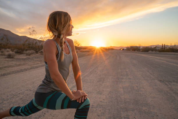 Young woman stretching body after jogging, sunset at the end of the road.