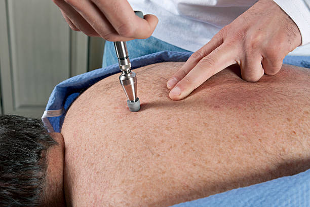 A chiropractor using an activator tool at the back of the patient.
