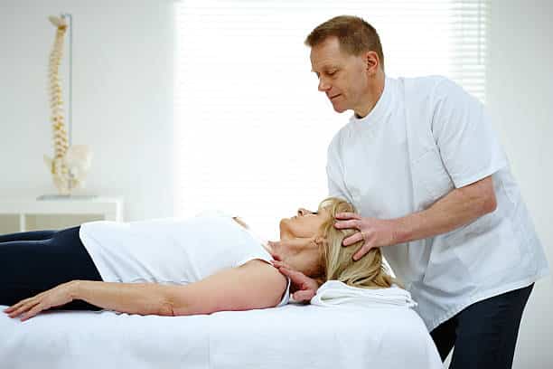 Chiropractor adjusting neck muscles of female patient inside the clinic.