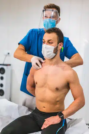 A physiotherapist with a screen and mask giving a shoulder massage