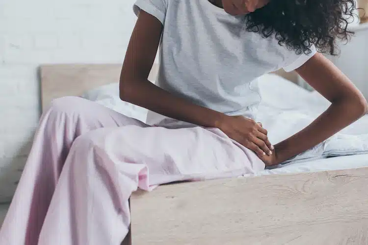 african american woman suffering from pain in hip while sitting on bed