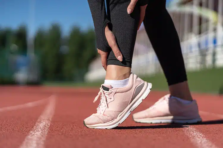 Jogger woman runner touching her foot in pain due to sprained ankle | foot and ankle pain treatment in columbus ne