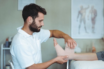 Chiropractor putting bandage on injured feet of patient to reduce the pain