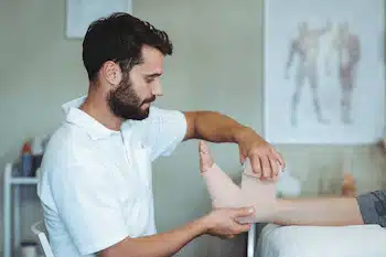 Chiropractor putting bandage on injured feet of patient to reduce the pain | foot and ankle pain treatment in columbus ne
