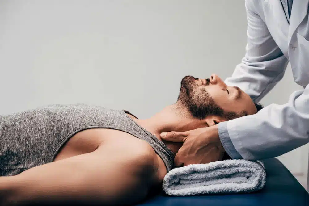 chiropractor massaging neck of man lying